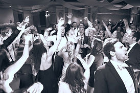 bride and groom singing in a crowd with their hands up in the air