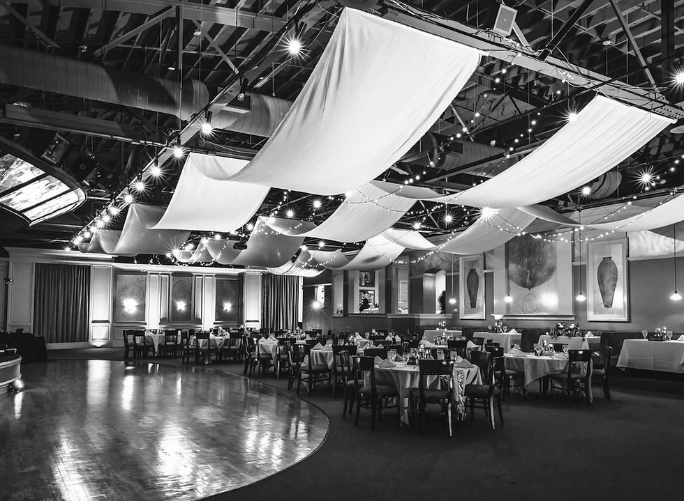 ride shot of reception room that has ceiling draping, ceiling draped string lights, a hardwood dance floor and stage
