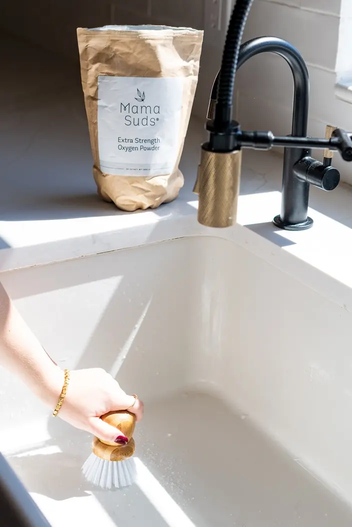 Thumbnail: Hand scrubbing white kitchen sink with wooden brush, "Mama Suds" bag nearby.