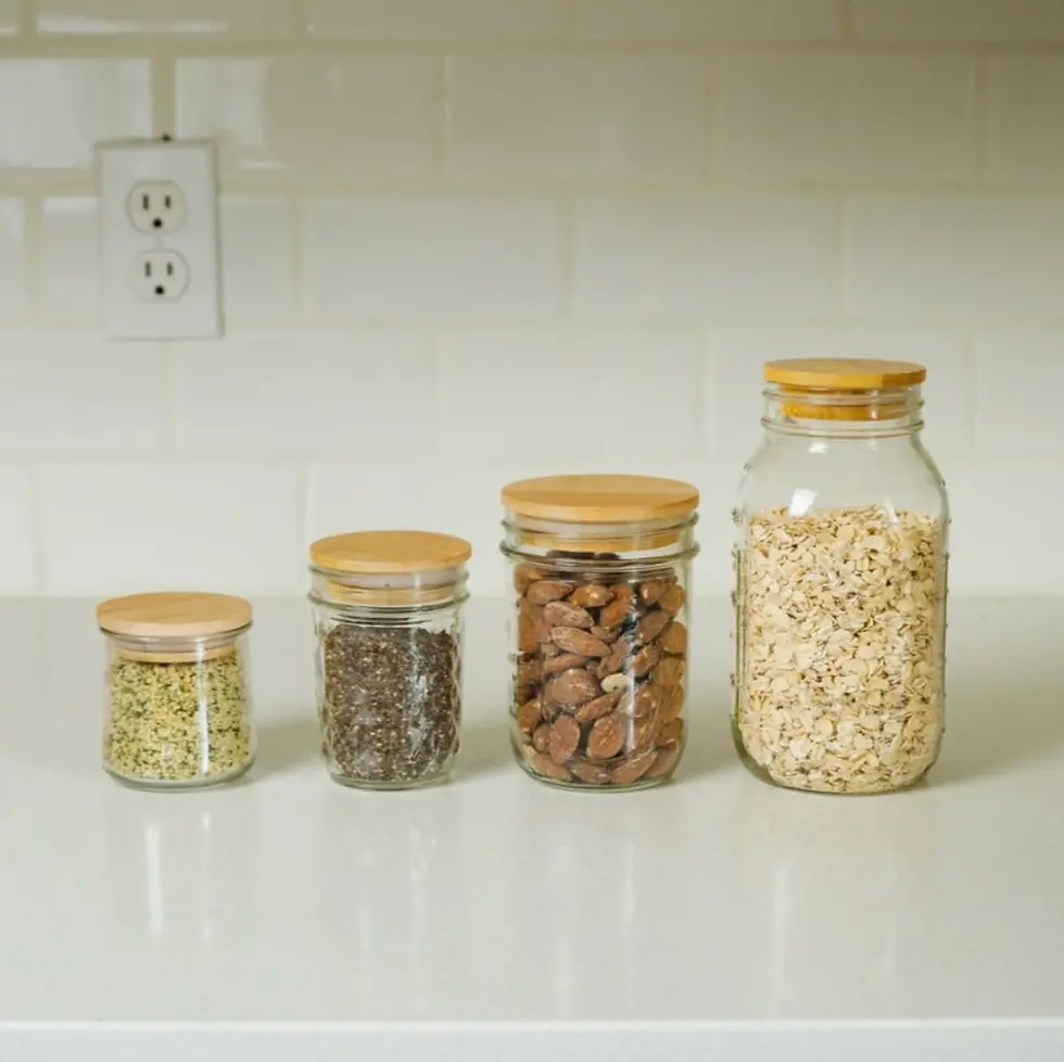 Thumbnail: Four glass jars with wooden lids, holding seeds, nuts, and oats.