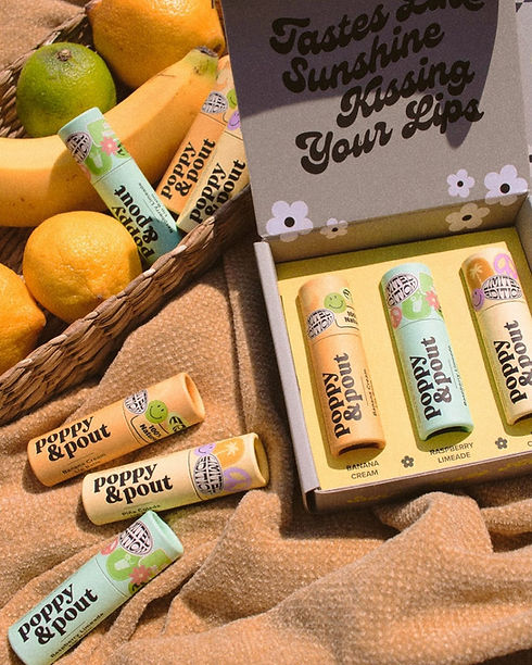 Photograph of Poppy & Pout vegan lip balms, displayed in a rustic basket with citrus fruits, presenting a variety of flavors.