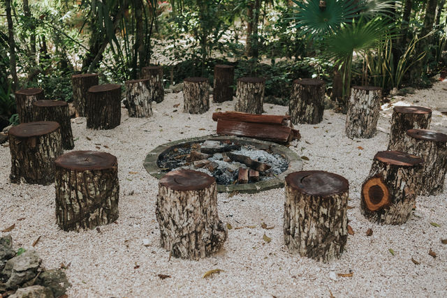 Rustic fire pit surrounded by tree stump seats at Lunita Jungle Retreat Center, Mexico, set amidst lush greenery for a tranquil gathering spot.