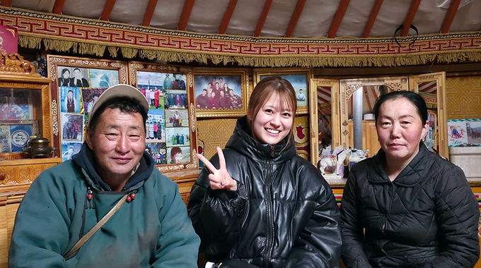 遊牧民のゲルの中で、ホストご夫婦と笑顔で記念撮影する女性旅行者(モンゴル遊牧民ホームステイ)