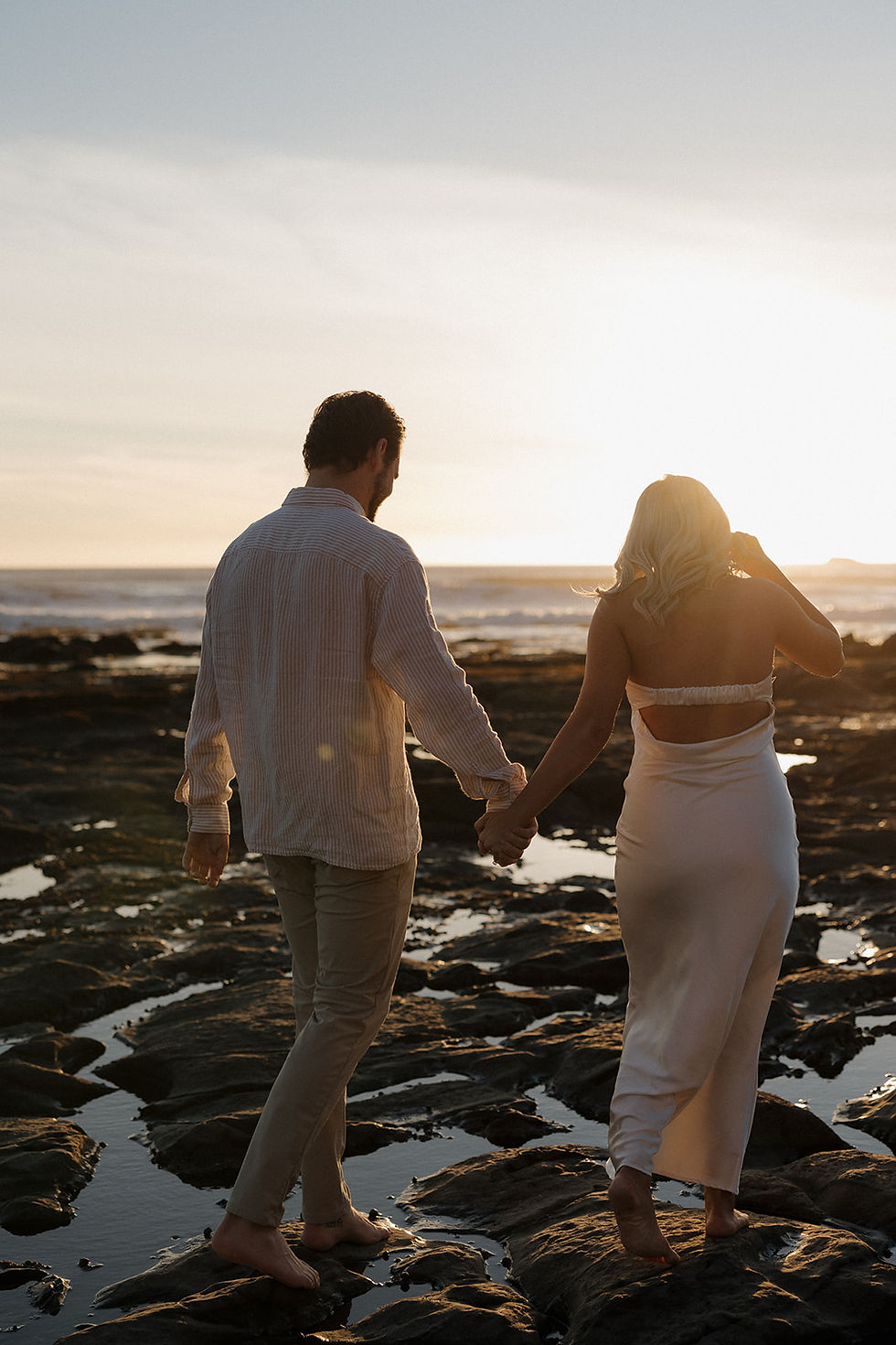 Couple walking barefoot along Shell Beach during sunset engagement session by San Luis Obispo Engagement Photographer