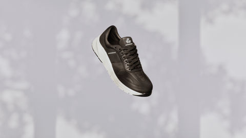 A brown sneaker with a white sole and laces is centered in front of a blurred background with silhouettes of trees. Through 3D animation, the shoe's design, featuring a logo on the tongue and brand name on the side, comes to life.