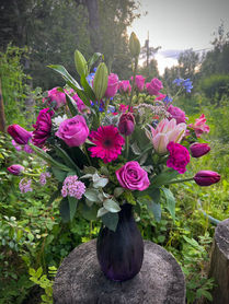 Fresh roses, tulips, and gerbera daisies arranged in a purple vase.