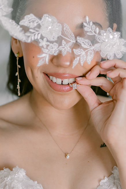 Bride smiling while holding up her engagement ring wearing a lace veil and delicate necklace, El Paso wedding photographer Photo by Jess