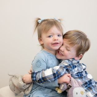 Siblings hugging while holding their beloved loveys during a Lovey & Me lifestyle photography session