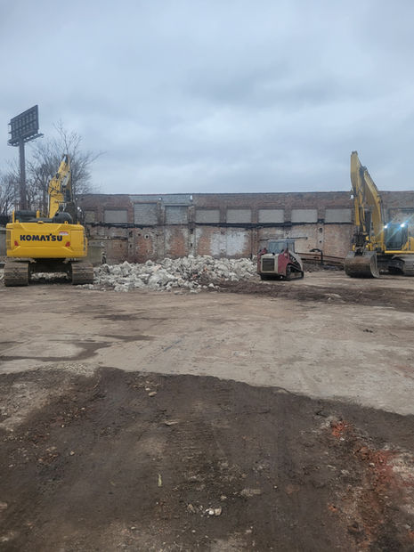 Two excavators on a cold day near a pile of stone at a job site.
