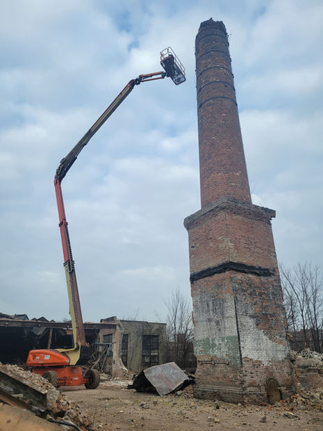 One of Brophy Excavator's professionals stand on the end of a crane truck to continue the demolition at a job site.