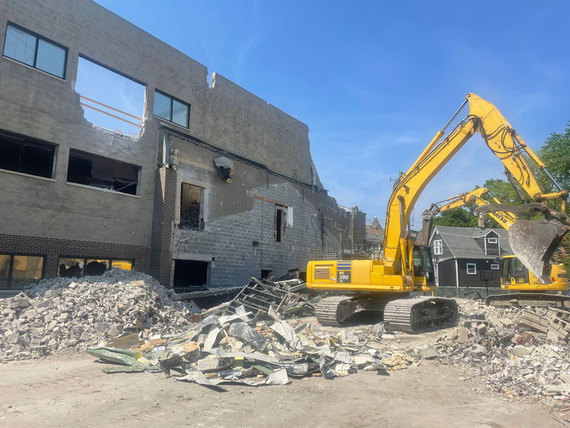 On a bright day, two excavators demolish a building while placing rubble, cement bricks, and garbage in appropriate piles.