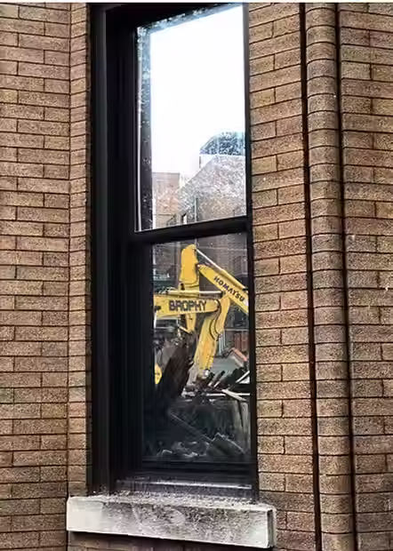 Through a window, multiple excavators demolish a job site.