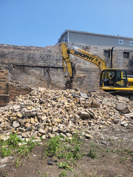 An excavator demolishing a building with large piles of bricks nearby.