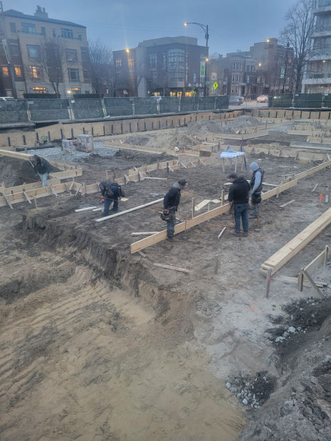 On a cold day, five Brophy Excavation experts in their coats are working at a job site with wooden shoring.