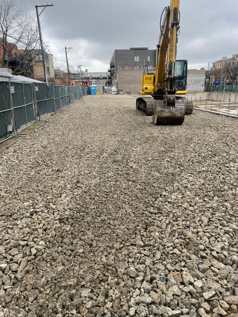 An excavator can be seen doing a final passthrough on ensuring the layers of stone are flat. Nearly off frame can be seen the superior grading done by Brophy Excavation.