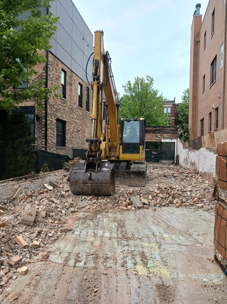 An excavator clears away bricks at a jobsite that is near completion. The neighboring buildings are unharmed.