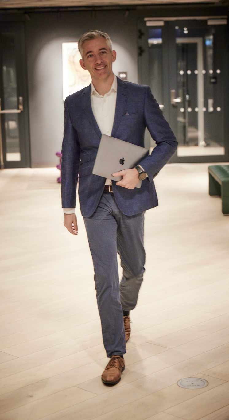 Dentist Jesper Hatt DDS dressed in a blue blazer walking along wearing a laptop in his hands