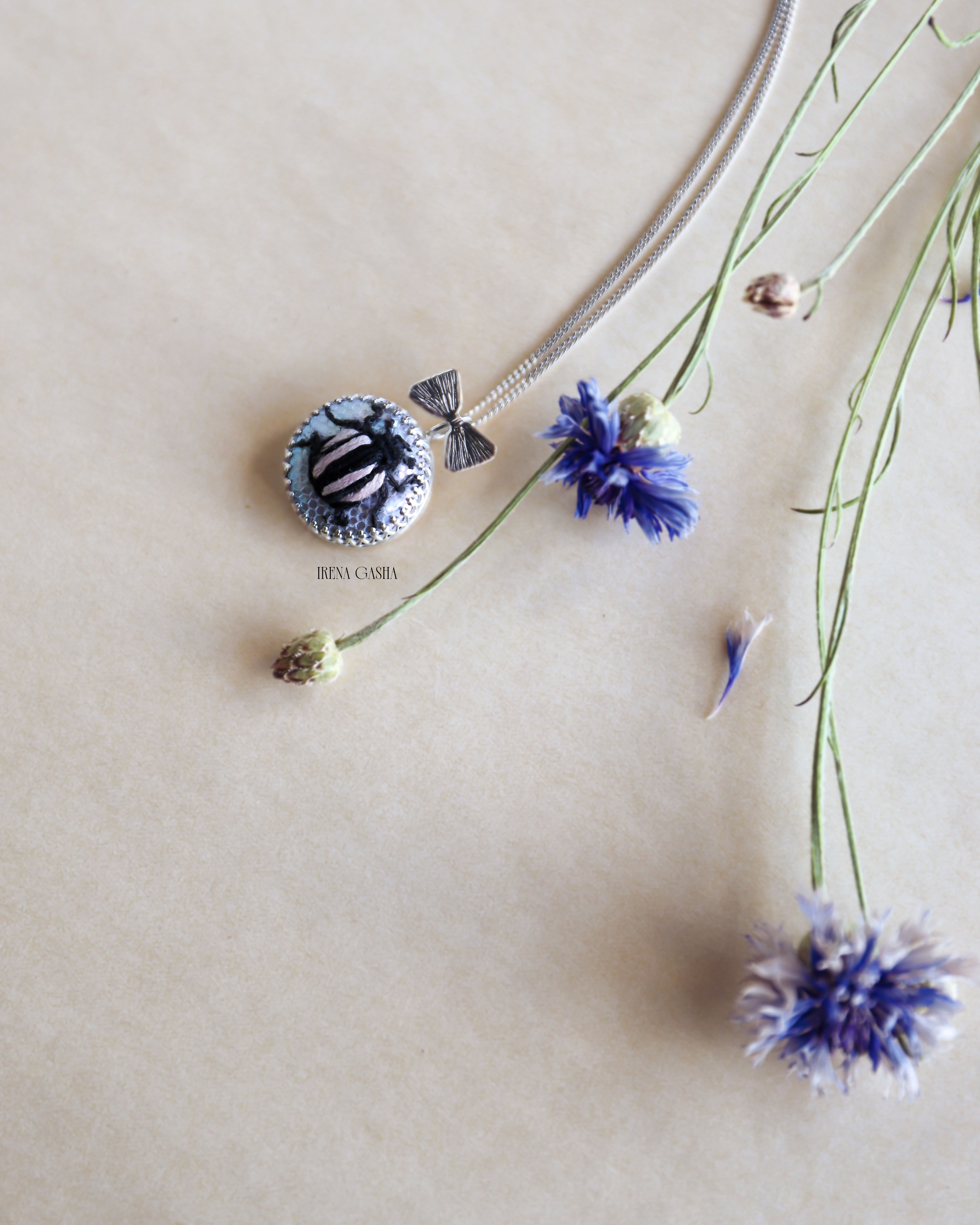 a hand-embroidered black beetle with soft pink-striped wings on a pearl in a silver setting with a silver bow accent