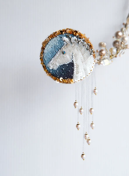 Hand-embroidered horse brooch with white sequins on a blue silk background, framed with gold beads 