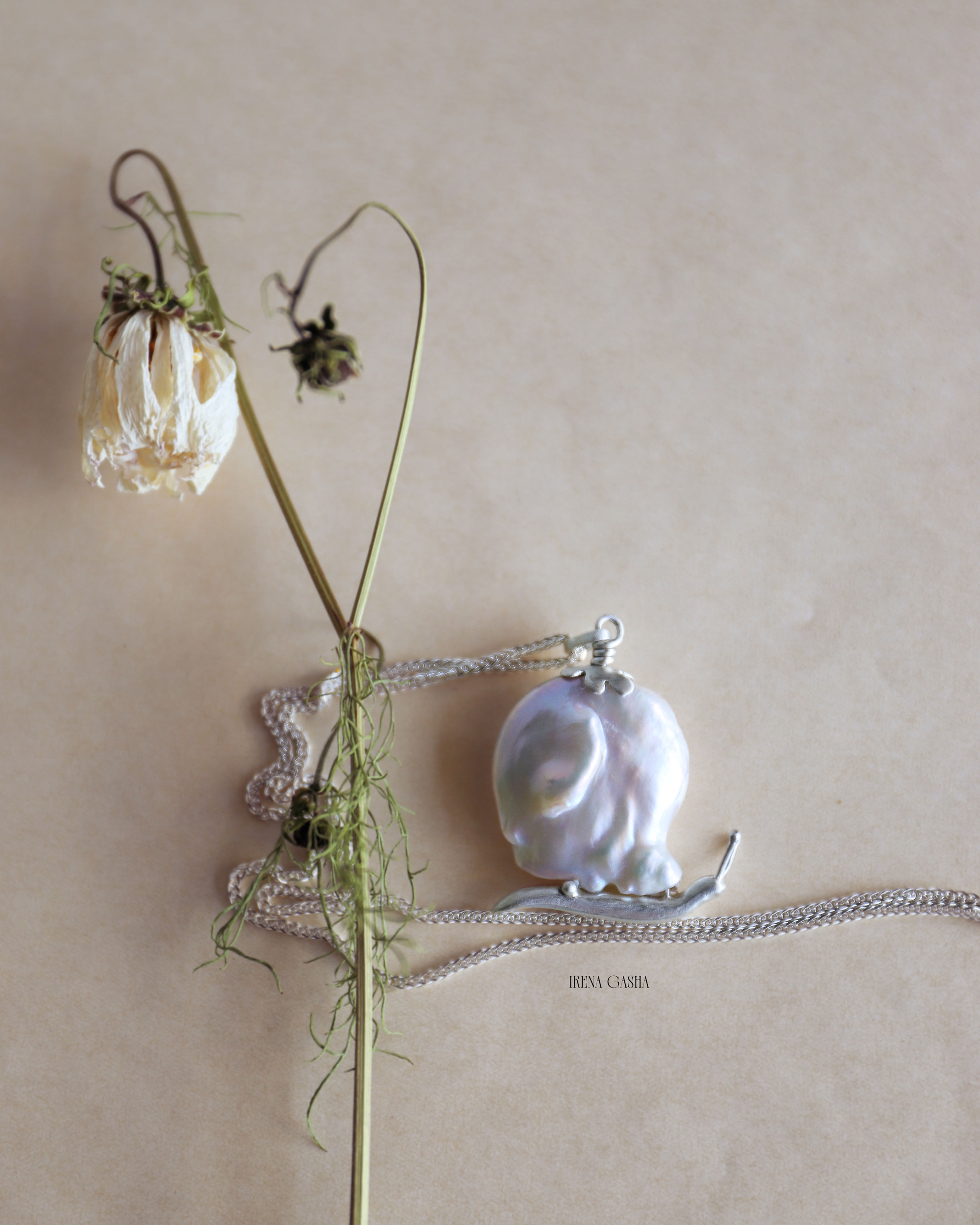 a baroque pearl shaped like a snail shell with a silver body and flower detail, on a silver chain