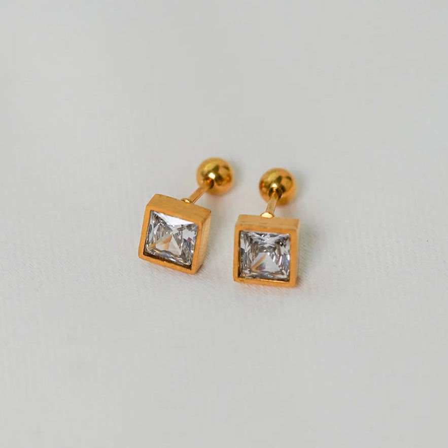 Gold square earrings with clear gemstones on a light gray background