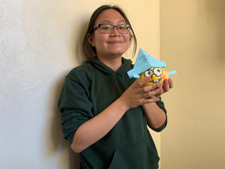 Alex is holding a yellow pumpkin that is painted as the character of Spongebob with the character's holes, big blue eyes, and buck teeth. The pumpkin also has a paper hat on it.