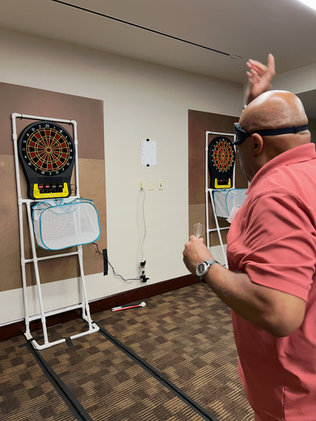 Position is taken from the left shoulder of a blind athlete wearing an eye mask as he throws a dart at an electronic dartboard. 