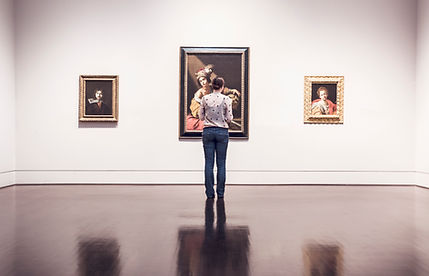 A person standing in a gallery in front of 3 paintings
צילום של אדם עומד בפני שלושה ציורים תלויים על קיר באולם או בגלריה