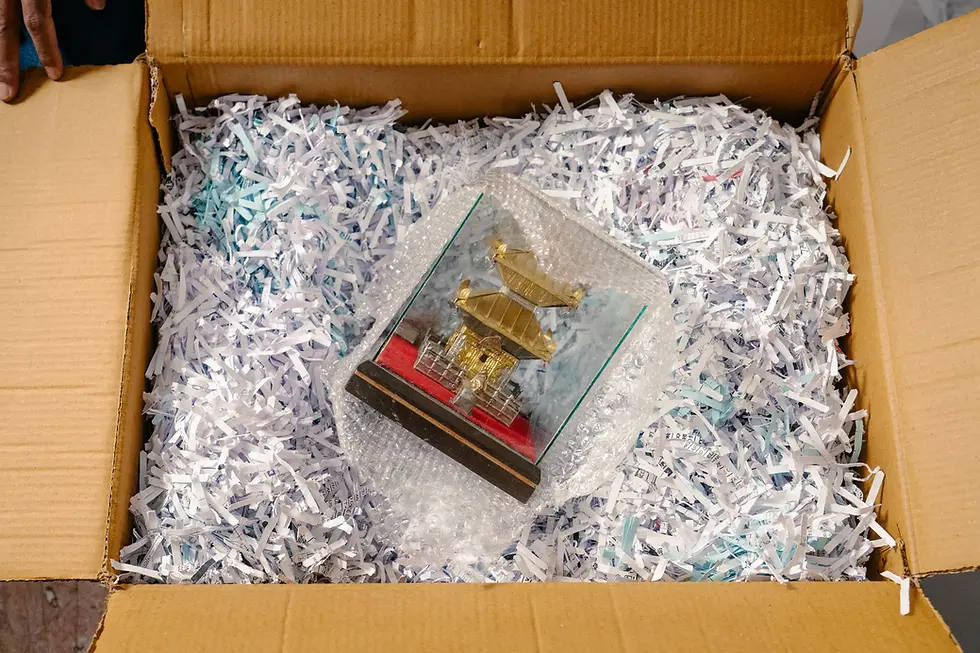 A small bronze model of a Nepali temple, nestled on some packaging bedding inside a brown box.