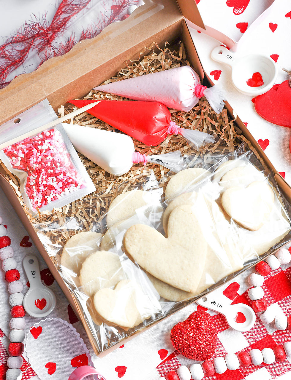 A staged undecorated DIY cookie kit for Valentine's Day called "Hearts Galore".  The kit includes 3 colors of royal icing and 6 heart shaped cookies. The cookies are boxed.