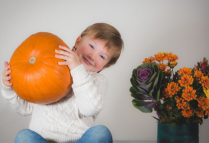 Elegant toddler posing smiling, holding a pumpkin and sitting on a table in an elegant home setting during a family photoshoot by Pennypics Photography