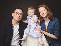 Young parents photographed with their baby daughter in a London studio against a dark background.