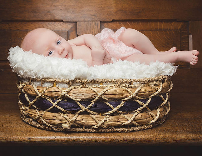 Newborn baby resting in a woven basket during an at-home newborn photoshoot in London, photographed by Pennypics with warm tones and carefully crafted light.