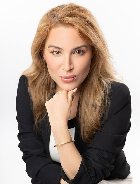 Full professional studio headshot of a confident woman with long blonde hair, wearing a stylish black and white business dress with a blazer. The subject is posed with her arms crossed, looking directly at the camera, conveying professionalism and executive presence against a clean white backdrop.