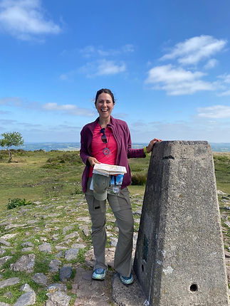 Walking leader standing with a trig point in the Mendip Hills