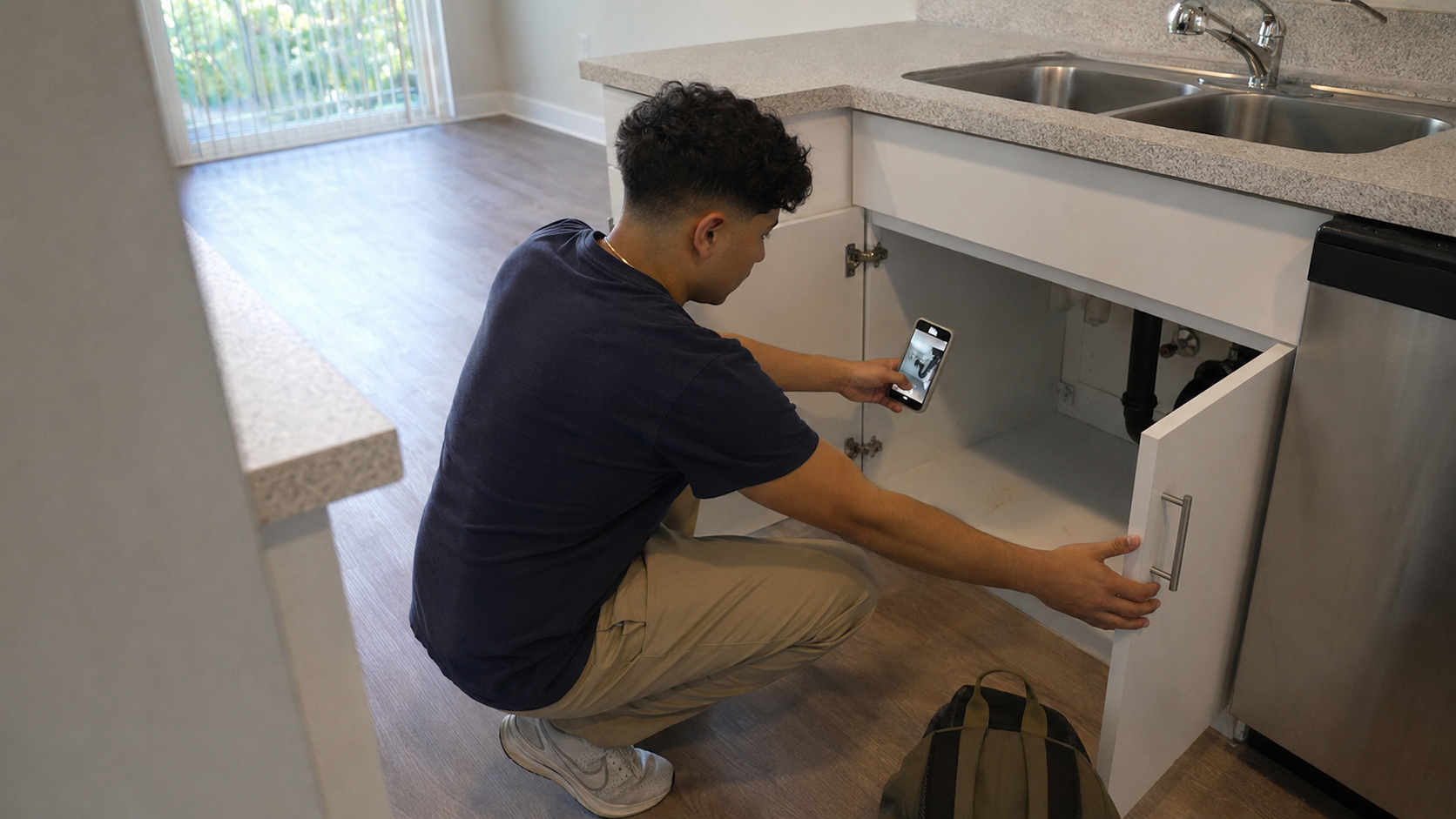 Young renter photographing the plumbing beneath a kitchen sink during an Orlando apartment tour