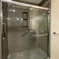 Tub to shower conversion with smooth Onyx walls, recessed caddy, grab bar, brushed nickel shower fixtures, and bypass clear shower door. 