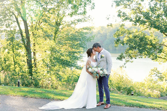 A bride and groom standing in front of Lake Galena with their foreheads touched together.