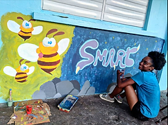 A woman sitting on the groun painting a mural with the word Smart written on a wall of a school