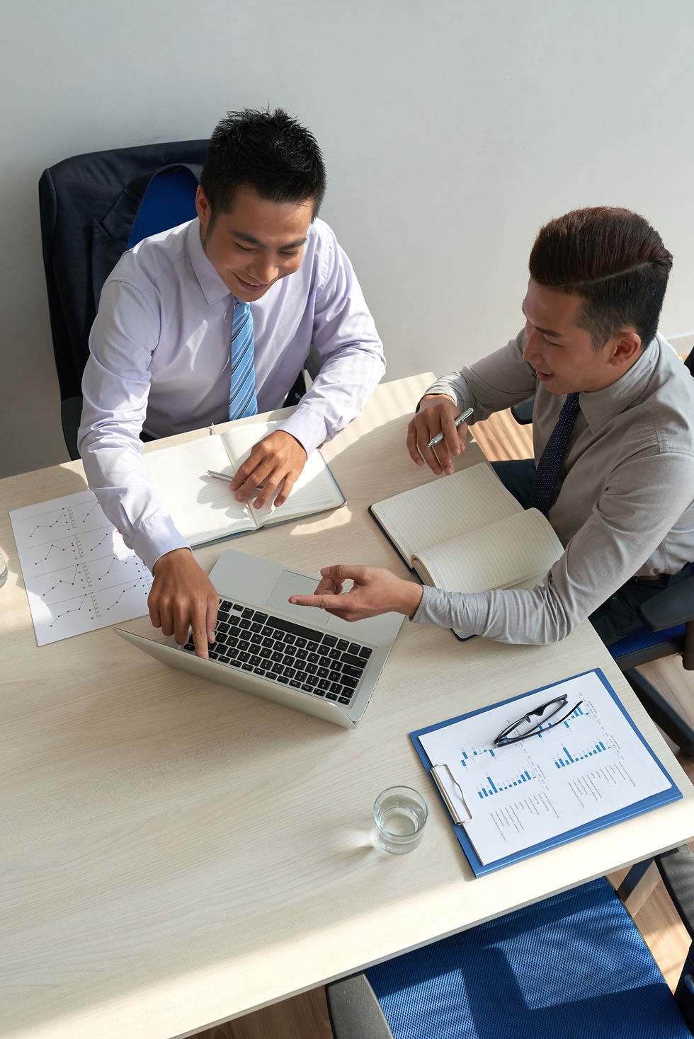 Two men in shirts looking at a laptop and documents on table