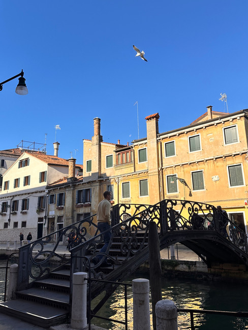 Petit pont de Venise sous le soleil, silhouette masculine en pull jaune beurre traversant la passerelle.