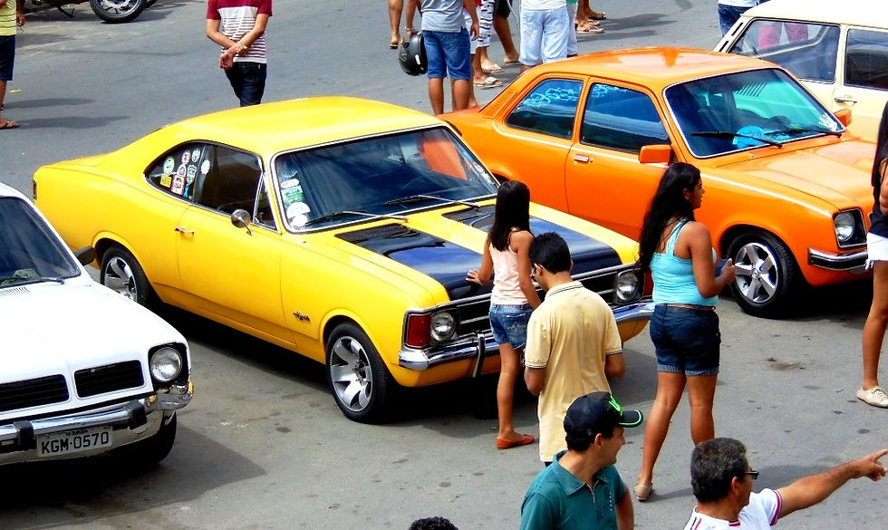 Carros antigos estacionados e pessoas observando.