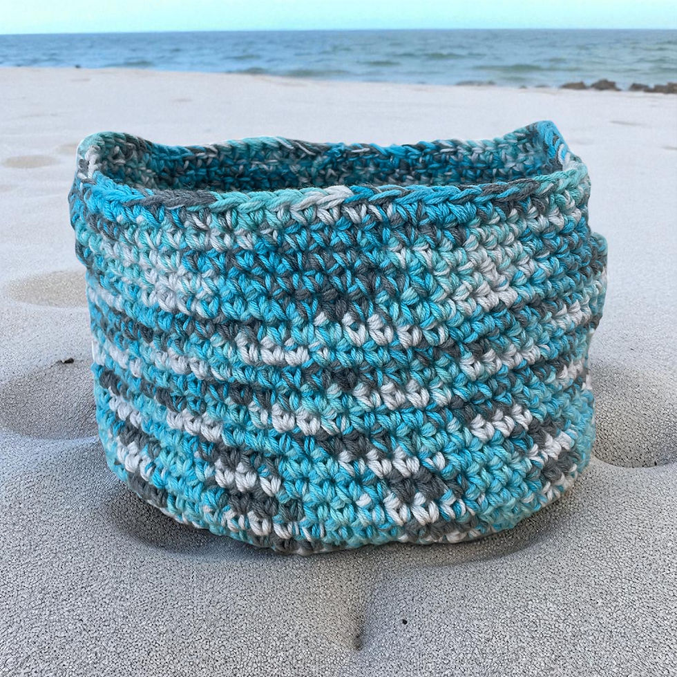 Blue and white crochet basket on sandy beach with the ocean background.