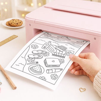 Impressora rosa imprime página de colorir com cenário fofo; mão segura a folha sobre mesa com cookies e materiais de papelaria.