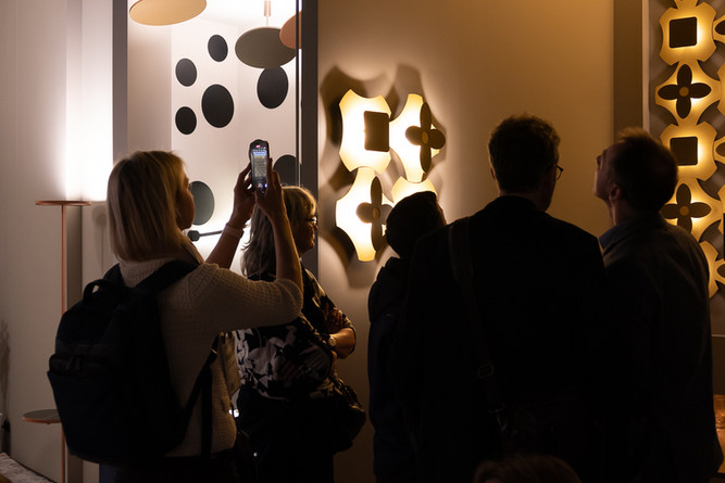 Frau fotografiert goldene Wandleuchte auf Messe