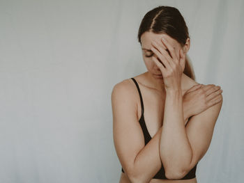 Frau mit weißem Hintergrund, hält sich eine Hand vor den Körper, die andere an den Kopf; Psychosomatik