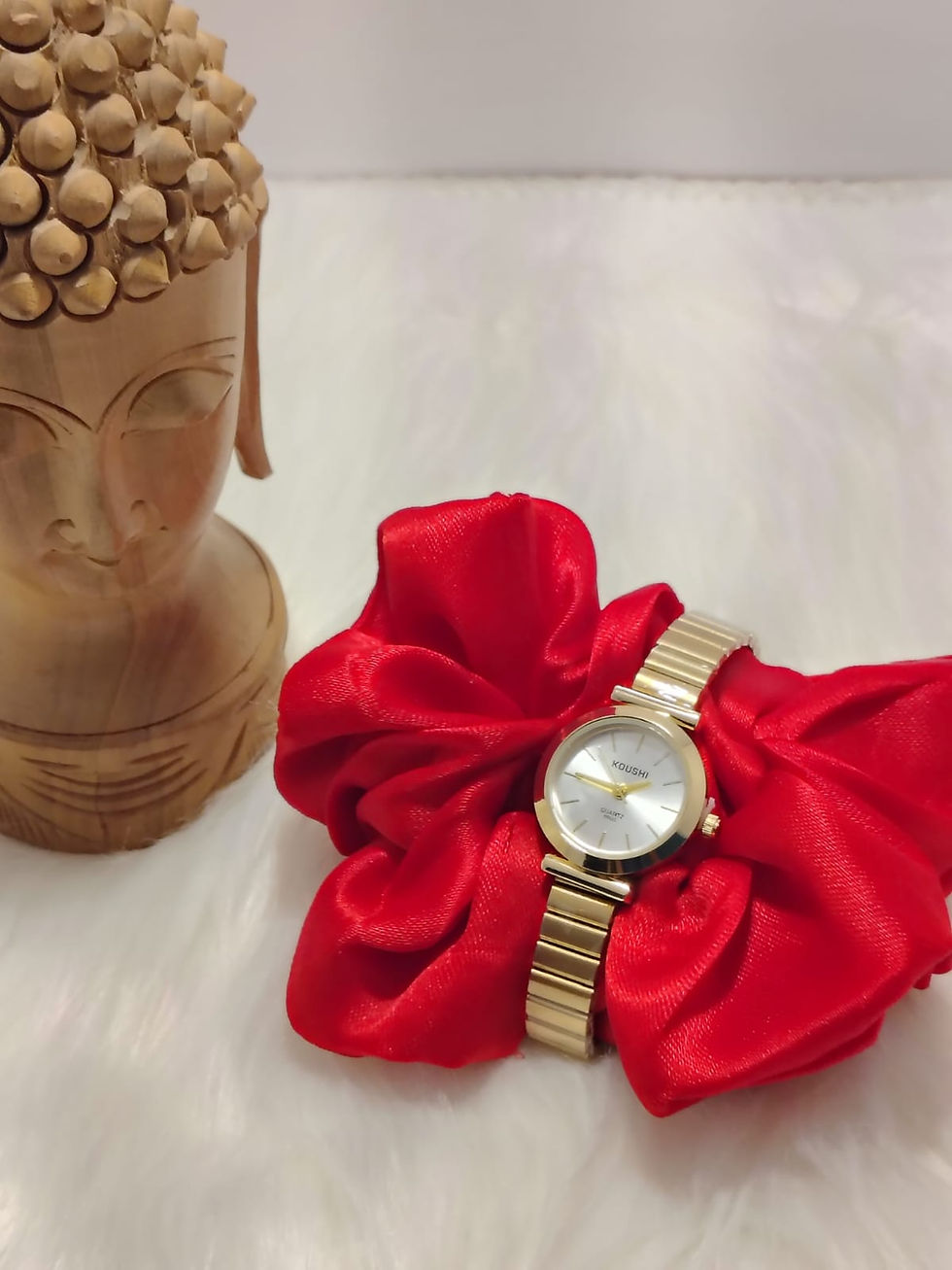 Small round dial watch on red fabric next to Buddha bust.