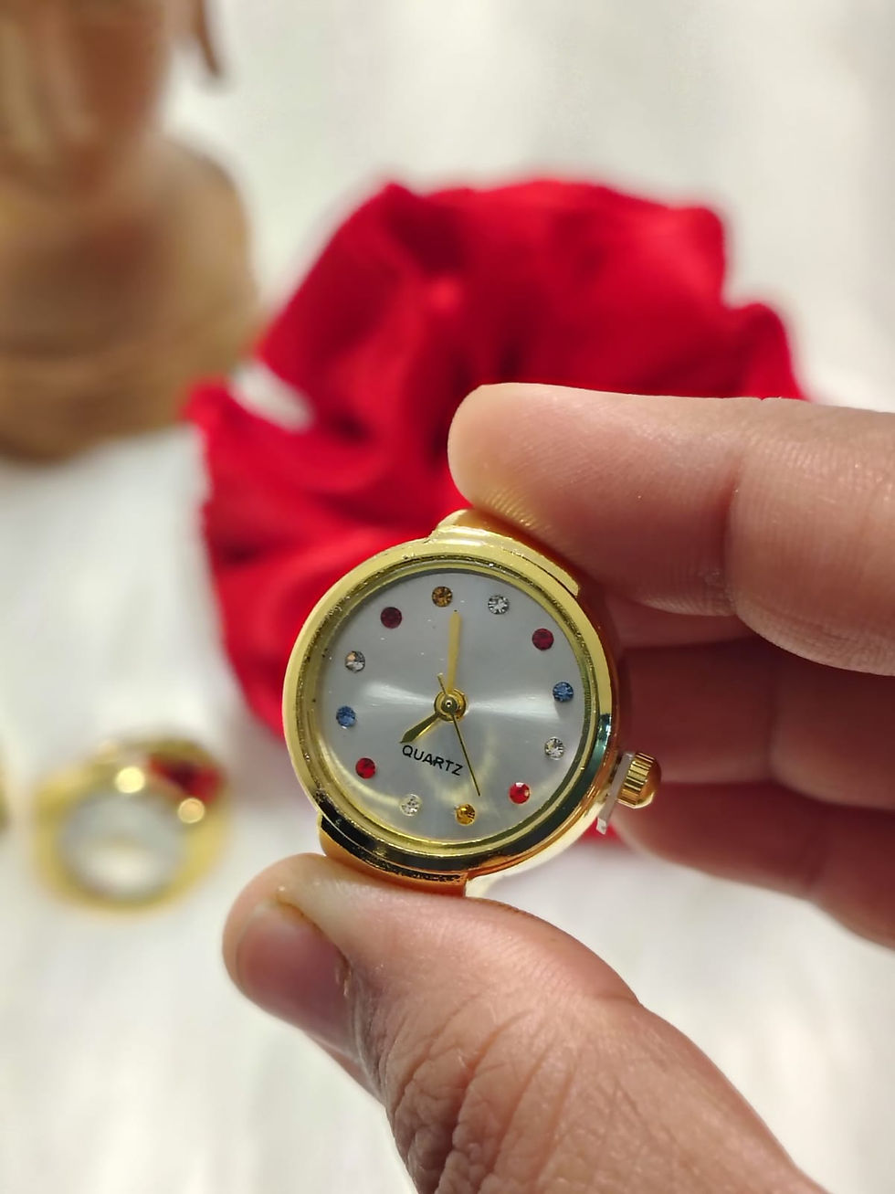 Gold multi colour ring watch held between fingers