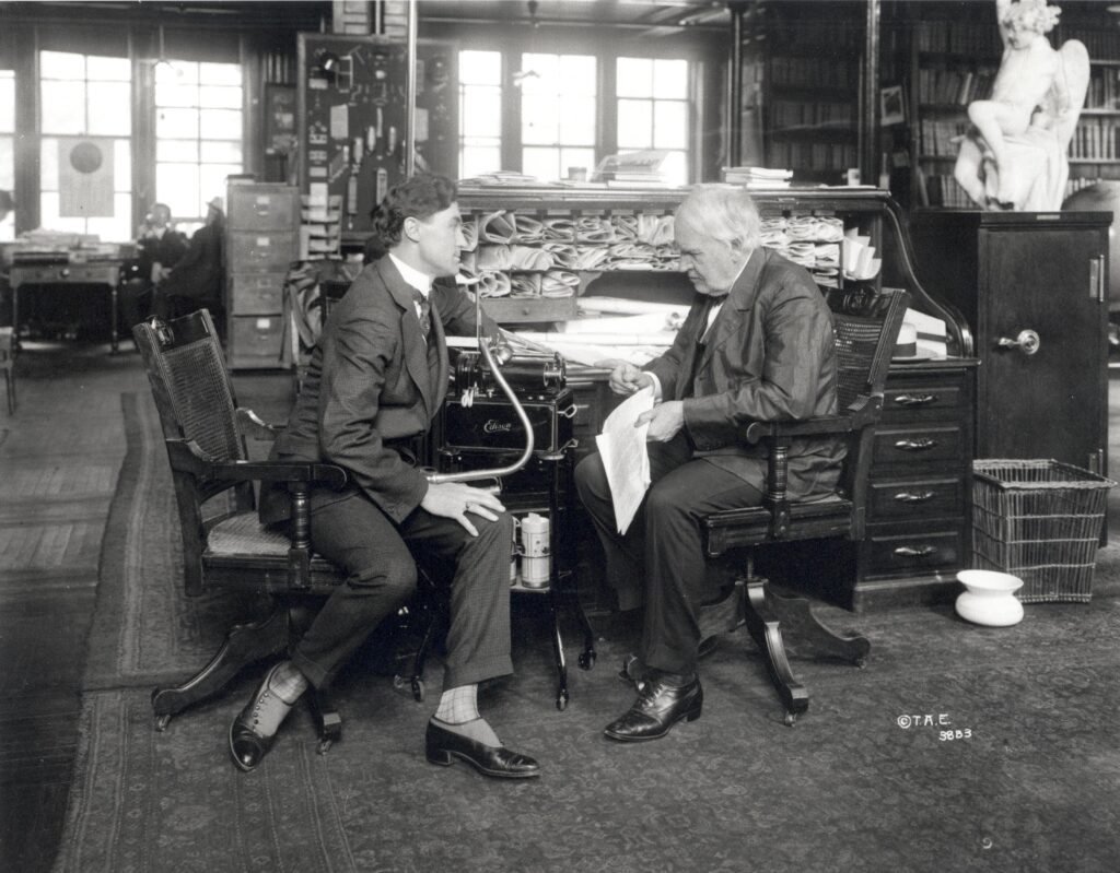 Like any good R&D organization, a capable staff keeping project managers aware of what is going on is indispensable. Here Thomas Edison confers with staff at his desk!