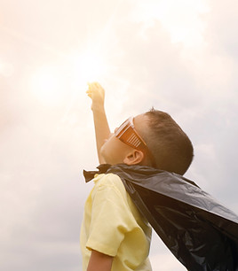 Young man pretending to be superhero reaching for sky.
